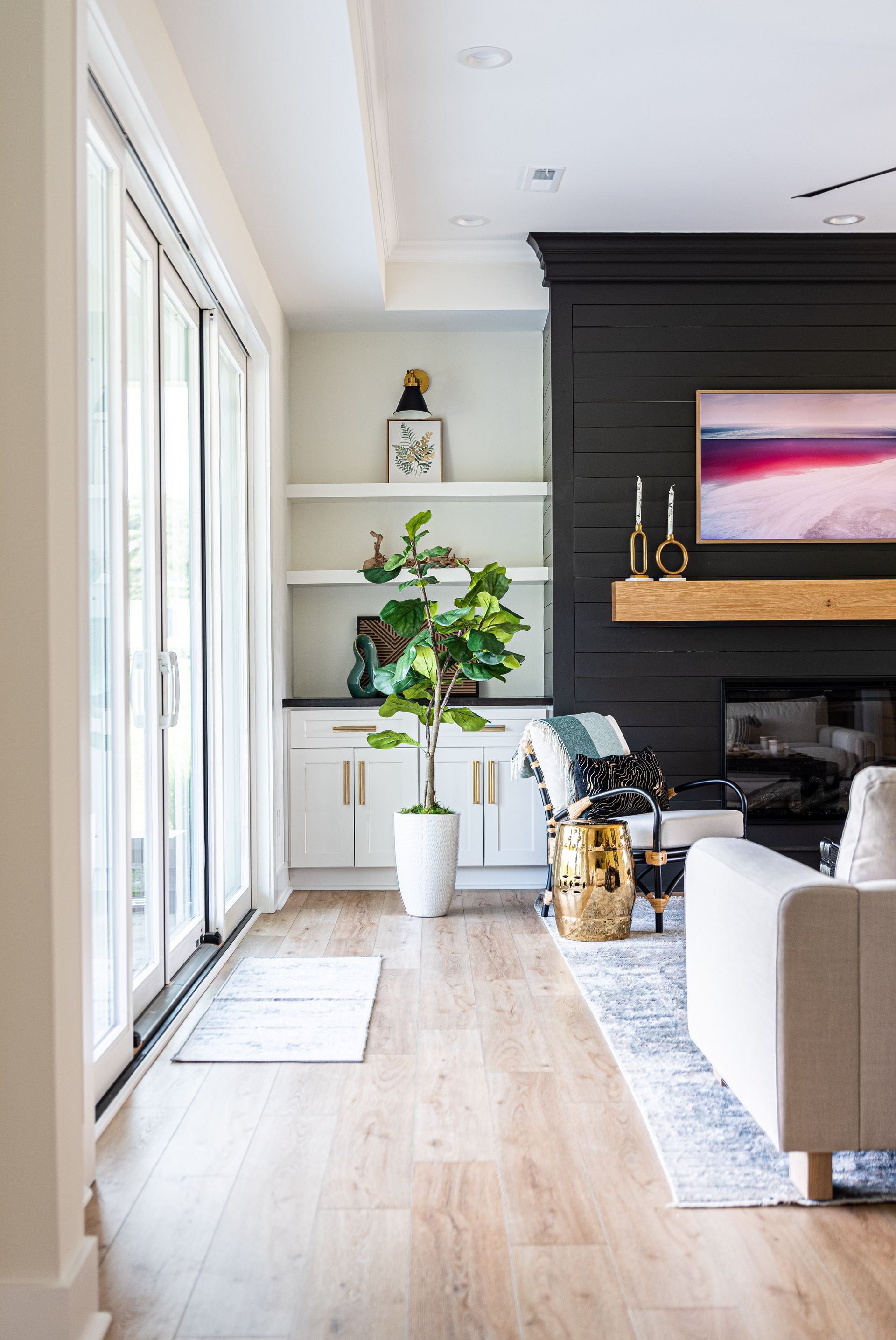Modern living room with black fireplace wall, large wall art, plants, and sliding glass doors