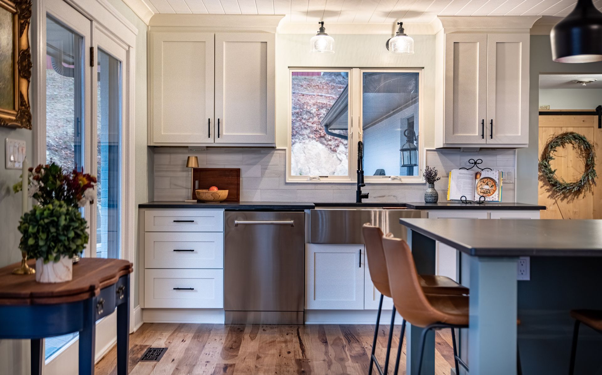 Bright modern kitchen with white cabinets, stainless dishwasher, window, and a blue island with stools
