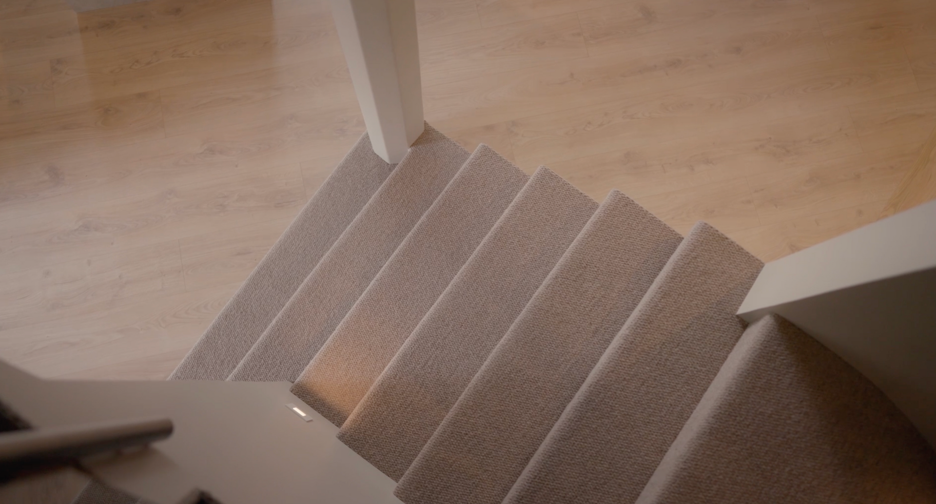Top of a carpeted staircase with white railings and light wood flooring.