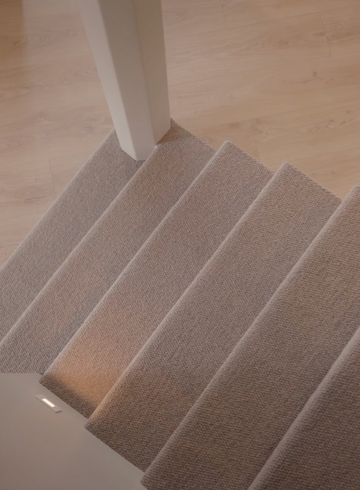 Carpeted staircase with white railing and light wood flooring at the top landing