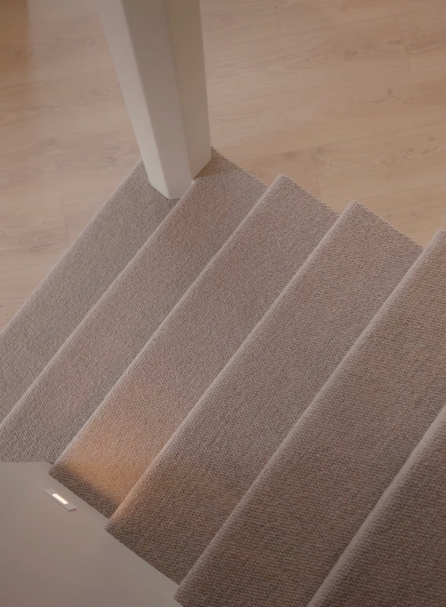 Carpeted staircase with light-colored steps and a white railing on a wooden floor