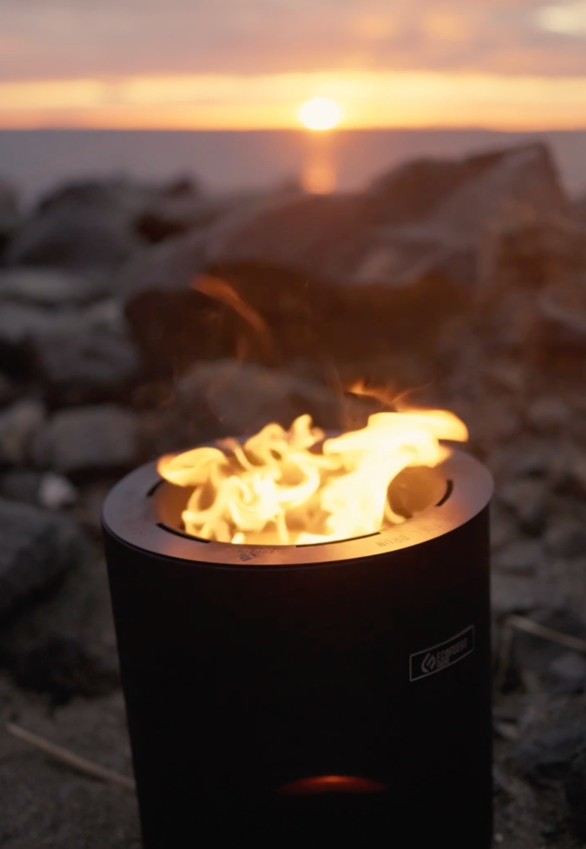 Small fire burning in a black fire pit at sunset on a rocky shoreline