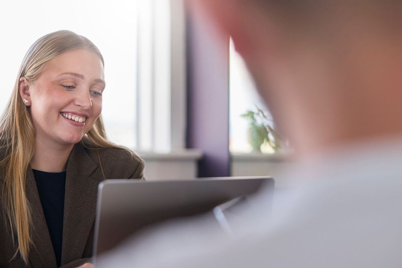 Smiling woman in a brown blazer talking across a table in a bright office