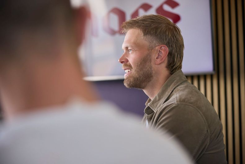Man speaking in profile at a presentation, with a blurred audience member in the foreground