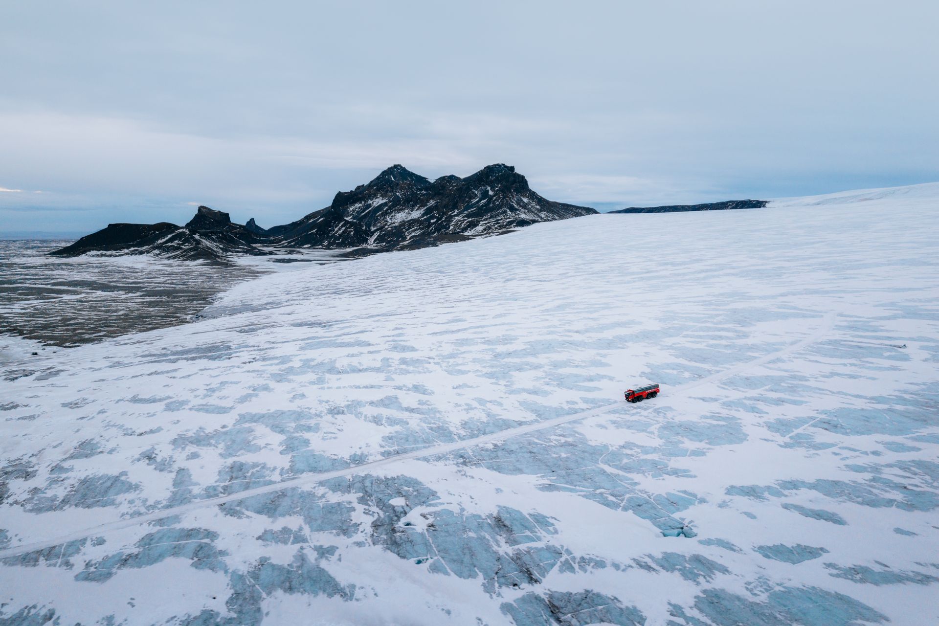 Snow-covered frozen landscape with dark rocky hills and a small red vehicle in the foreground