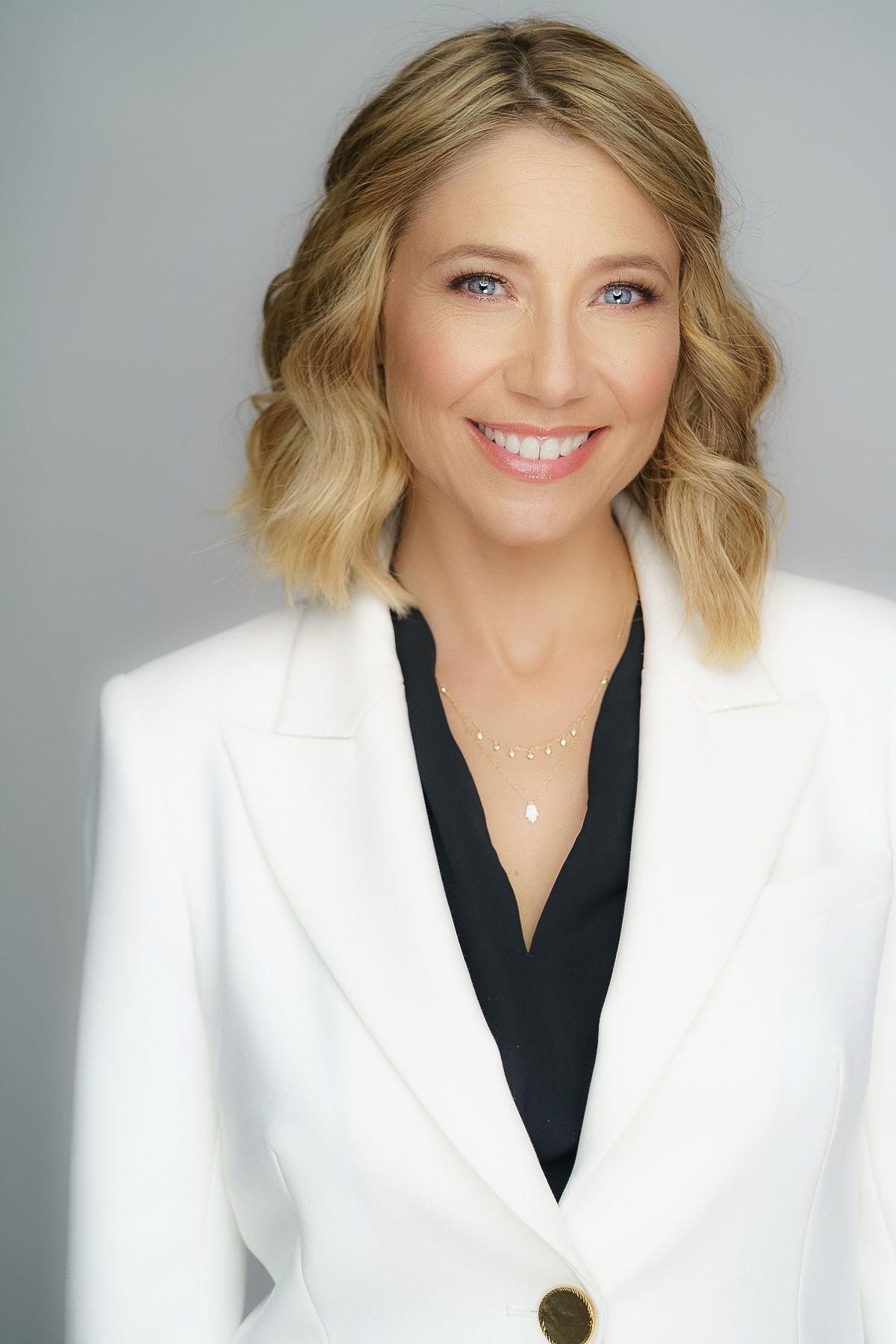 A woman in a white jacket and black shirt is smiling for the camera.