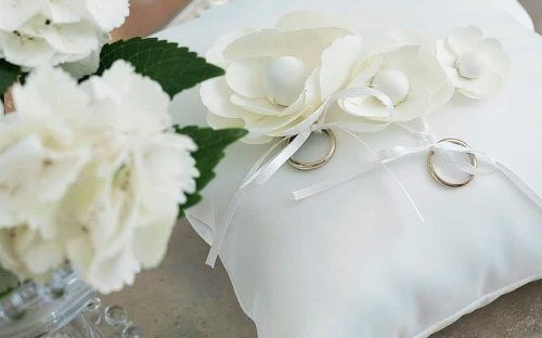 Un cuscino con sopra fedi nuziali e fiori.