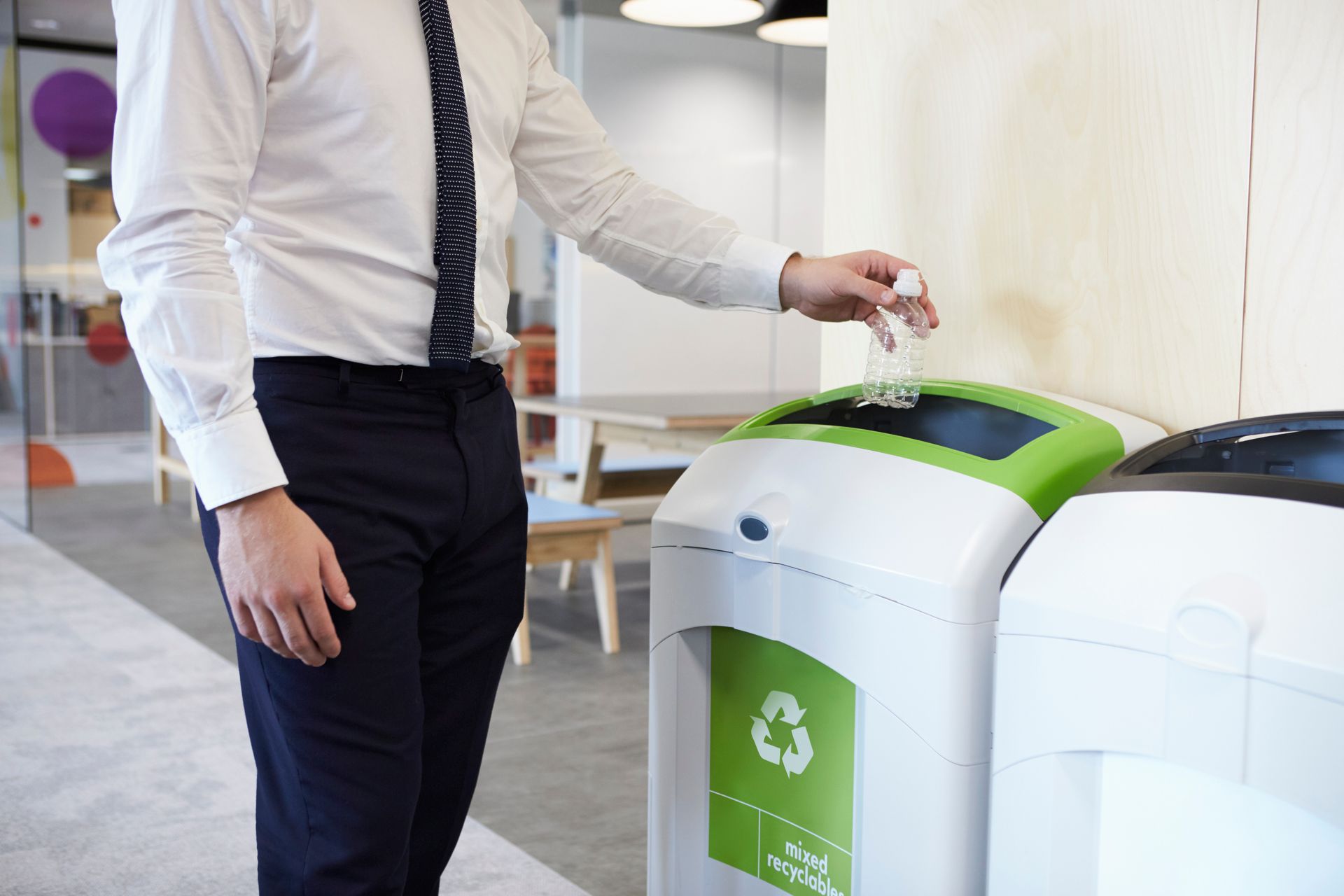 A man is throwing a plastic bottle into a recycling bin at his workplace.