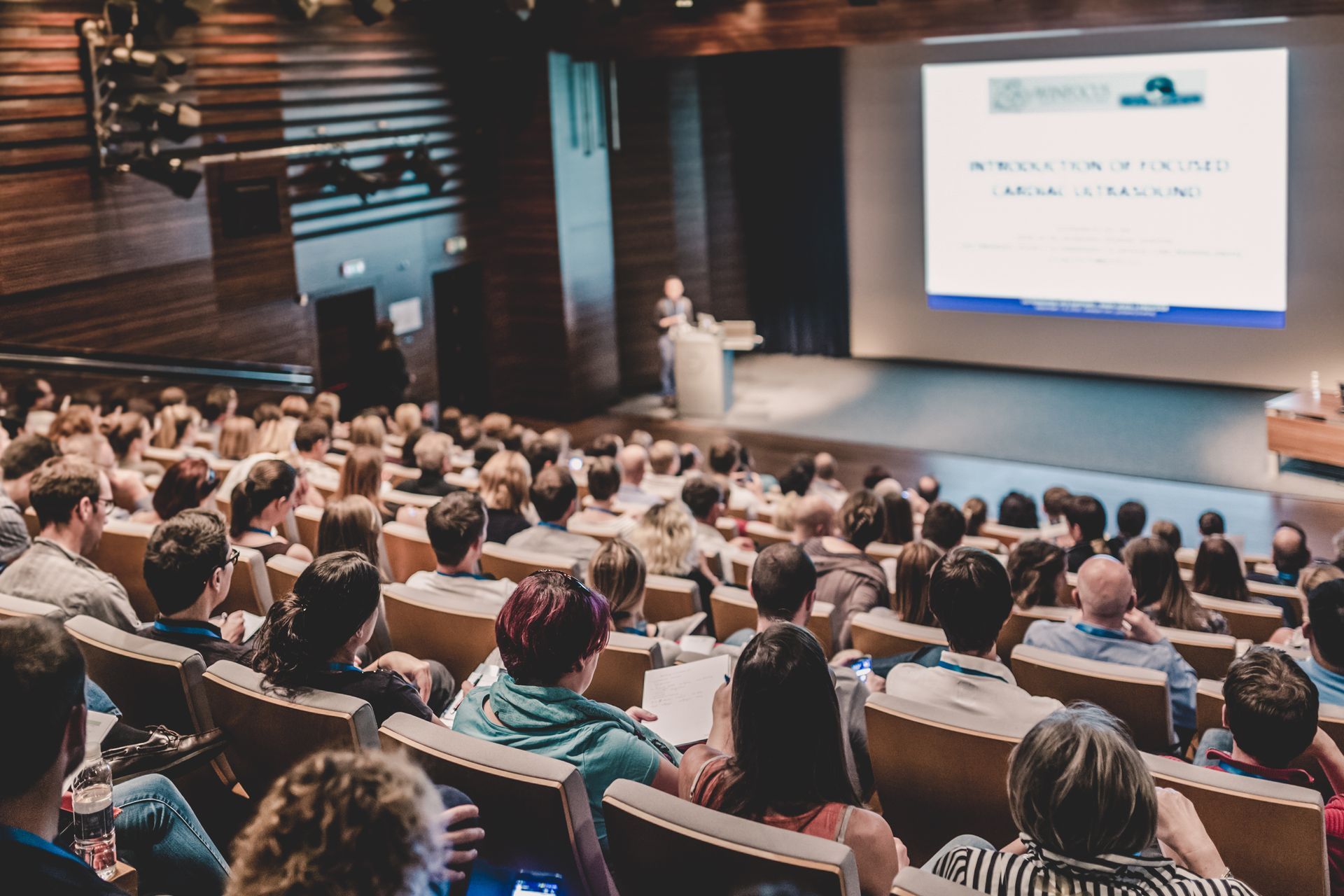 A large group of people are sitting in an auditorium watching a presentation.