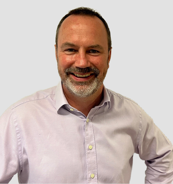 A man with a beard is wearing a purple shirt and smiling