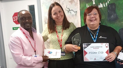 3 people smiling, 1 holding a certificate and award