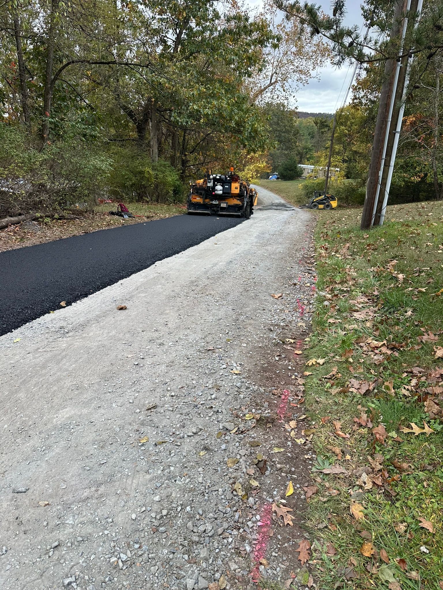 Black car on a newly paved road beside a gravel shoulder in a wooded area.