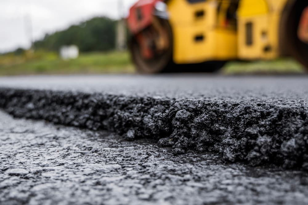 Close-up of freshly laid asphalt being compacted by a road roller on a road.