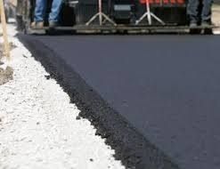 Fresh black asphalt being laid beside a white road edge line, with workers visible in the background