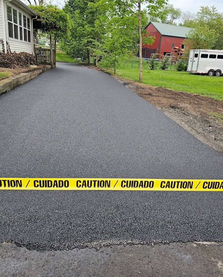 Fresh blacktop driveway with yellow caution tape across it beside a house and barn