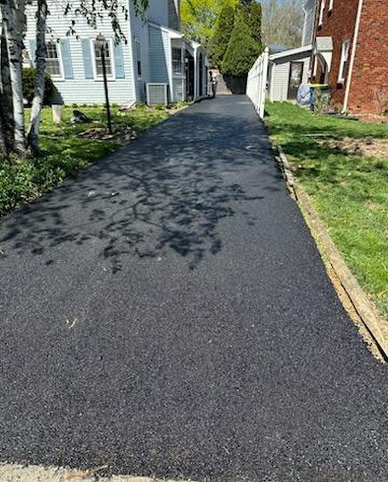 Fresh black asphalt driveway or lane between houses with tree shadows