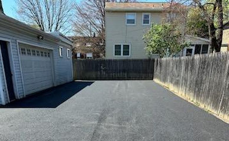 Empty asphalt driveway beside a garage, bordered by wooden fences and a beige house in the background