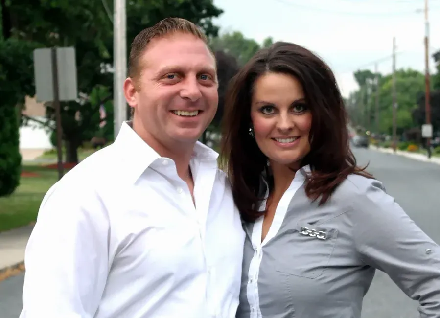 Two people smiling outdoors on a street, wearing white and gray shirts