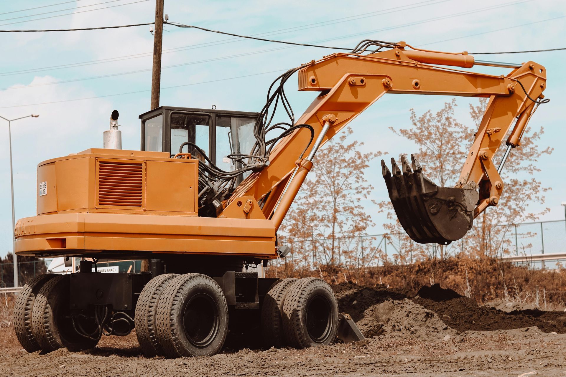 Orange excavator scooping dirt at a construction site with piles of soil and utility poles in the background