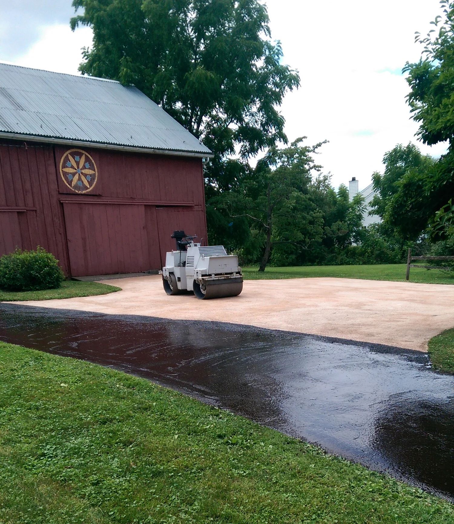 Small white utility vehicle on a gravel driveway beside a red barn and trees after rain