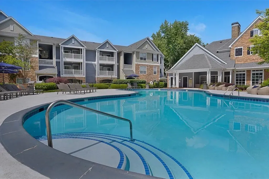 Resort-style swimming pool with lounge chairs and apartment buildings in the background.