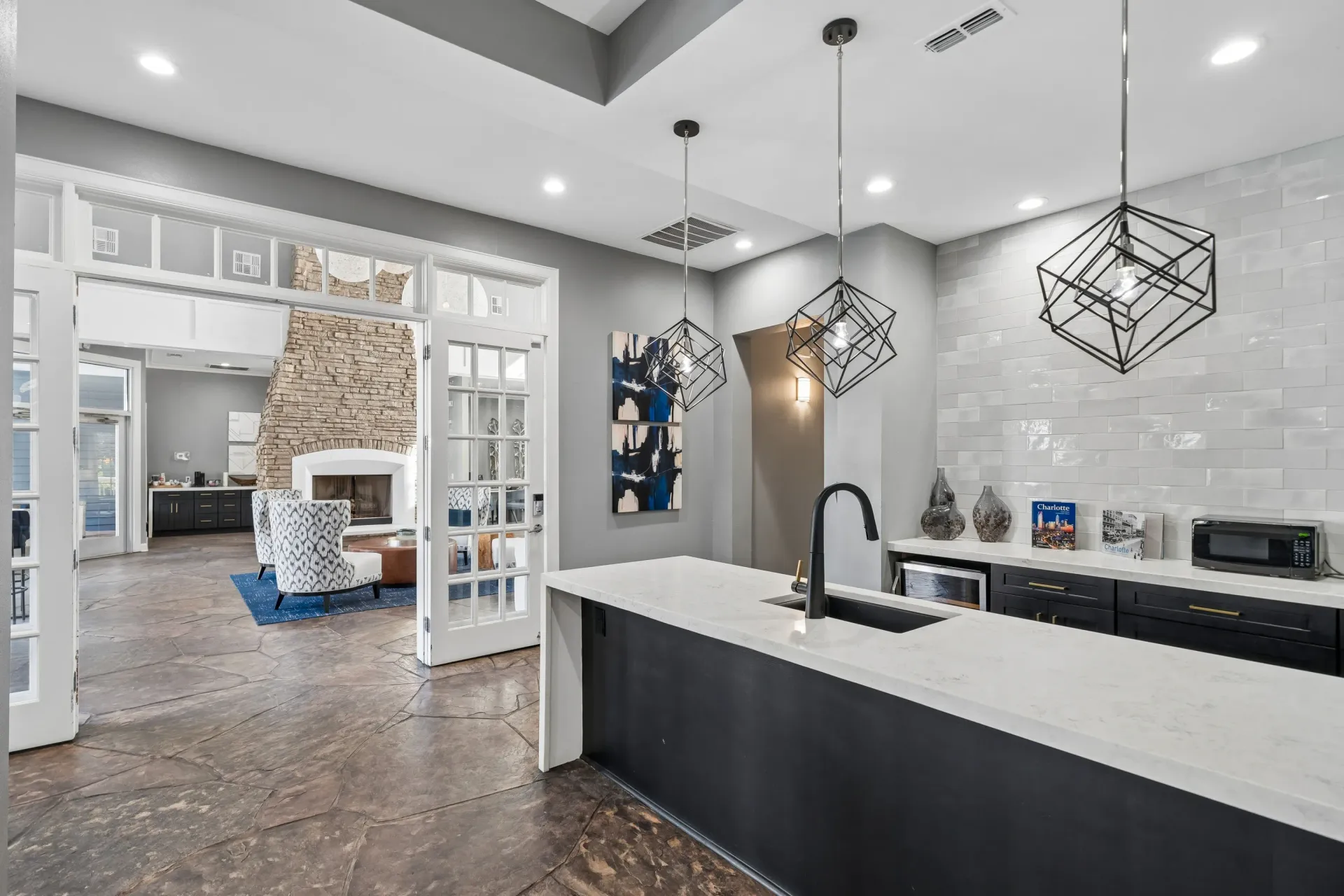 Modern kitchen island with a black faucet and white countertop, overlooking a lounge area with a stone fireplace.