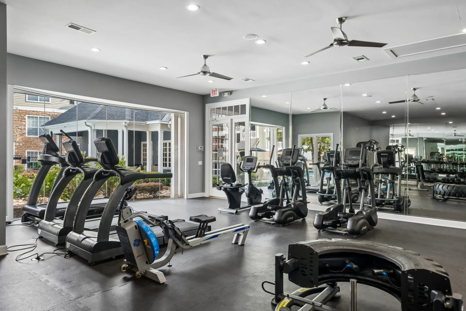 Fitness center with treadmills, ellipticals, rowing machines, and weight equipment, with large mirrors and an outdoor view.