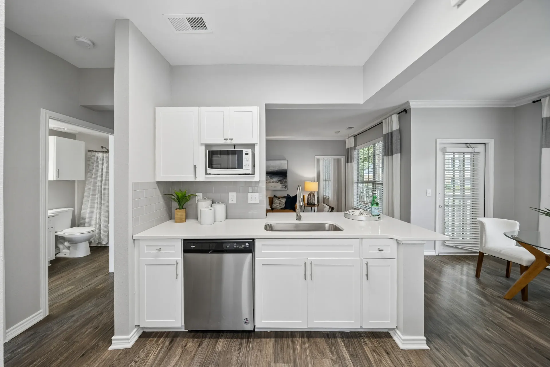 Modern kitchen with white cabinets, stainless steel appliances, and view of living room and bathroom.