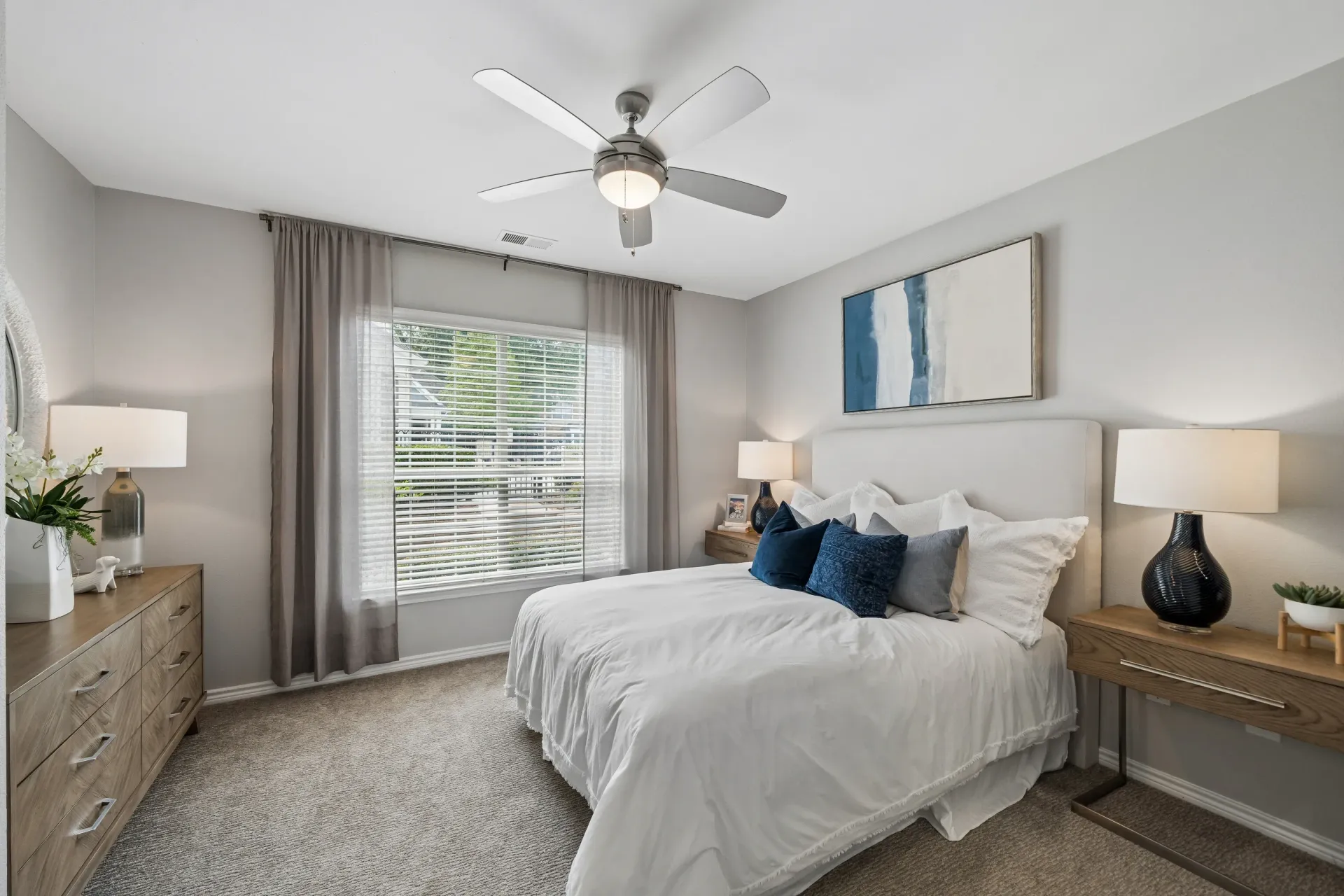 A cozy bedroom with a queen-size bed, nightstands, a dresser, and a ceiling fan.