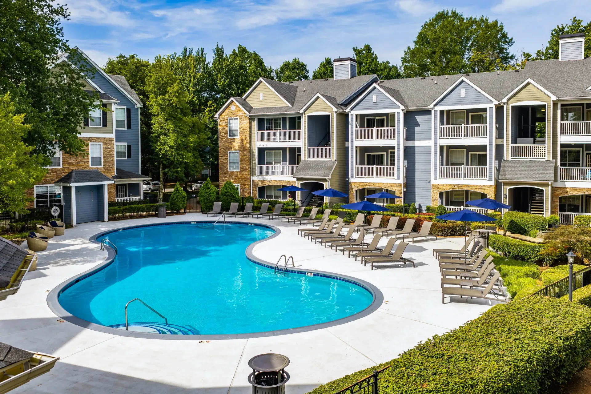 Resort-style swimming pool with lounge chairs and umbrellas at an apartment complex.