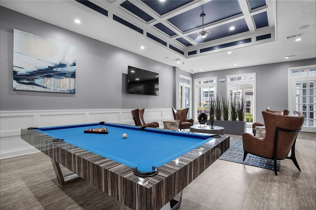 Indoor amenity room with a blue pool table, modern seating, a wall-mounted TV, and large windows at The Piedmont.
