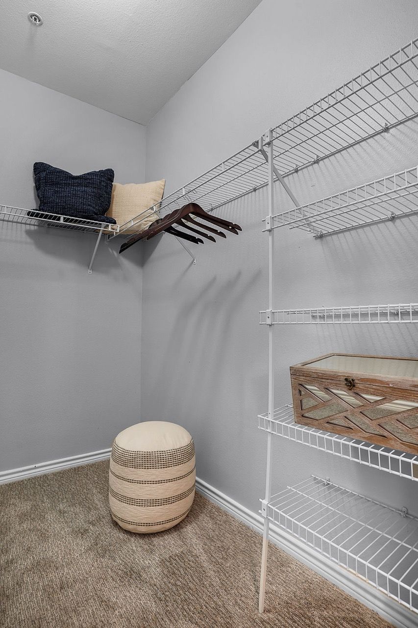 Walk-in closet with white wire shelving, clothing rods, and a round woven ottoman at The Piedmont.