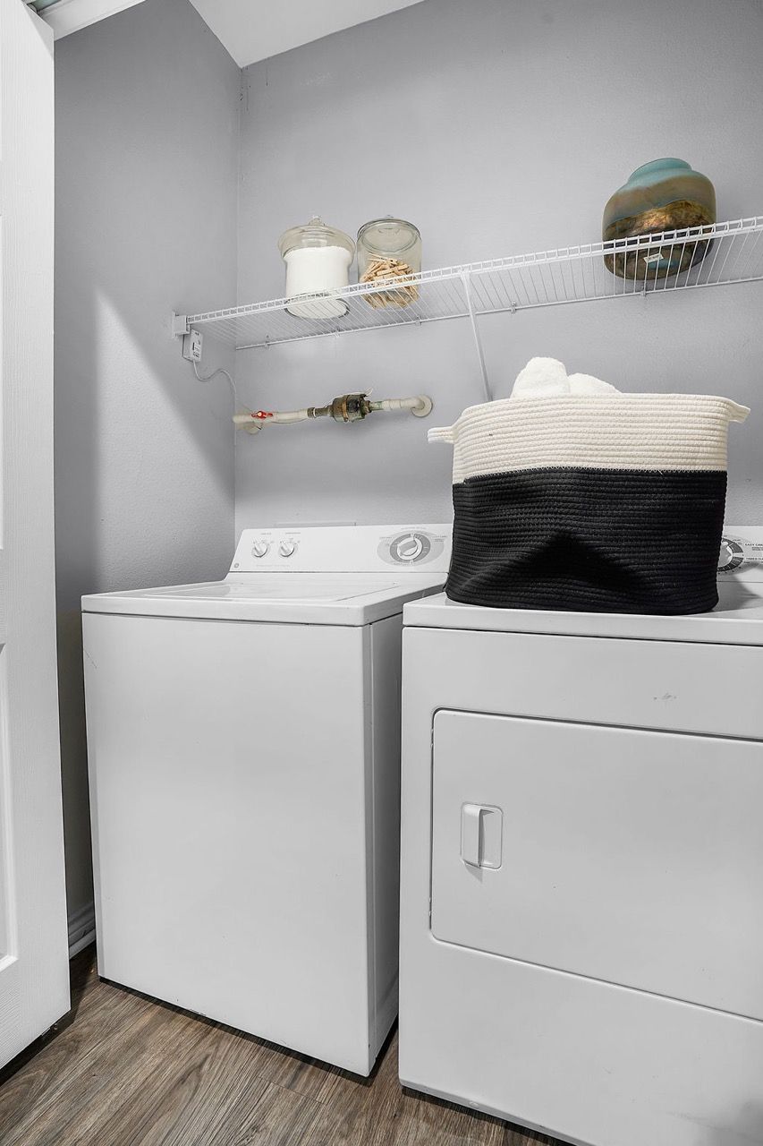 Laundry room with white washer and dryer side by side and a wire shelf above at The Piedmont.