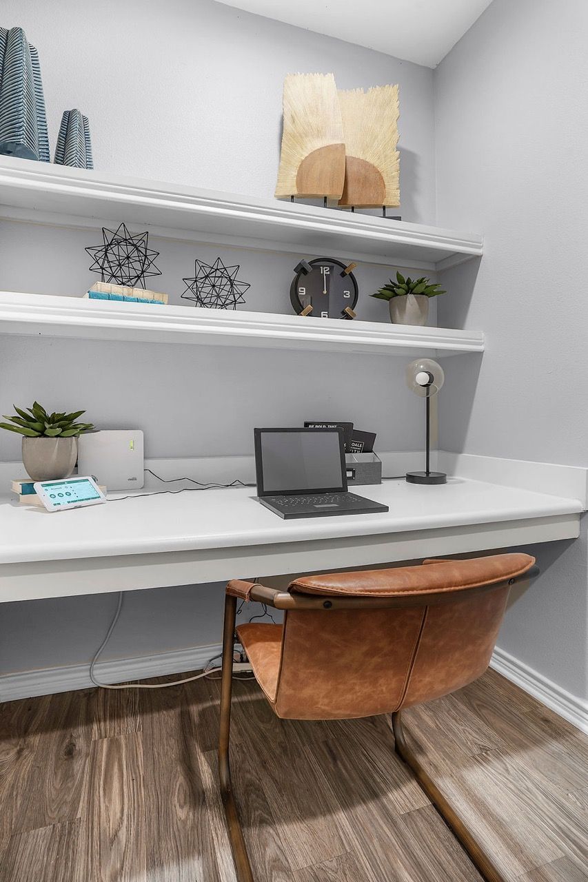Modern home office nook with white desk, laptop, desk lamp, shelves, and a brown leather chair at The Piedmont.