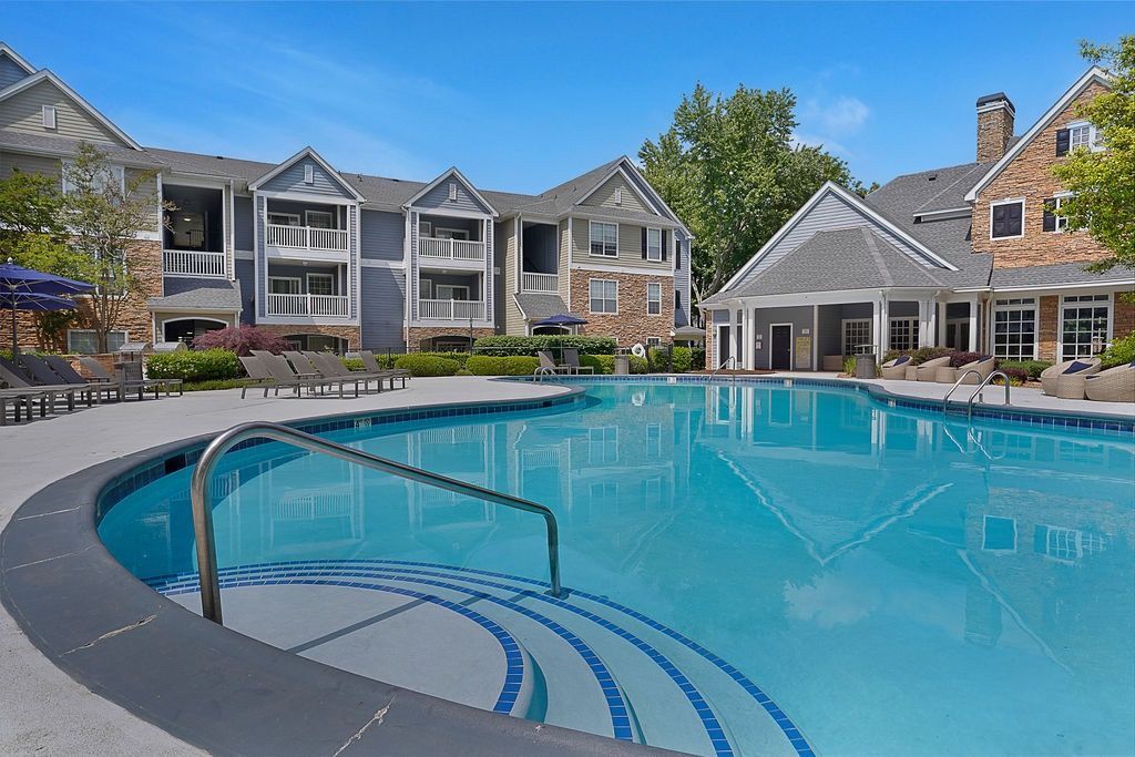 Outdoor community pool with curved steps and a metal handrail, surrounded by lounge chairs and apartment buildings at The Piedmont.