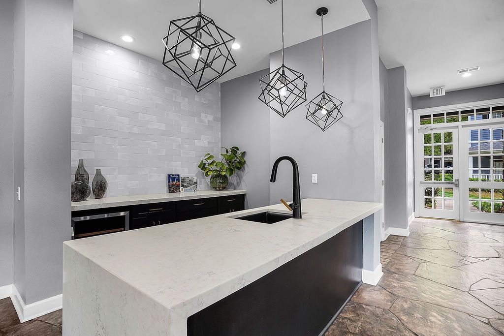 Modern community kitchen with a white island, black faucet, pendant lights, and glass doors at the entrance at The Piedmont.
