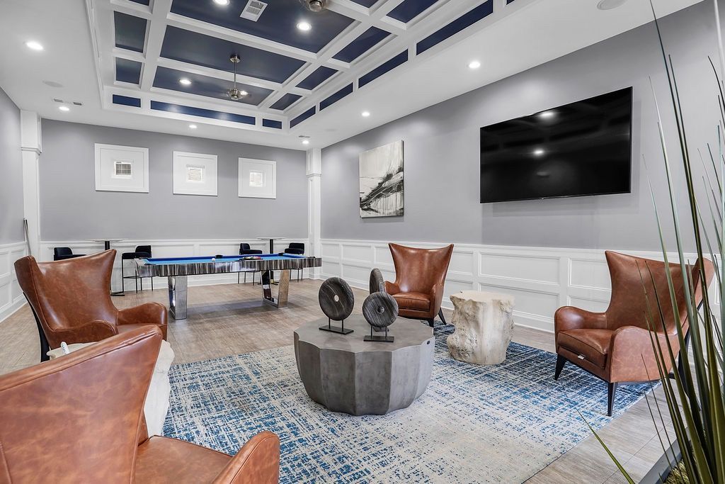 Modern resident lounge with a pool table, brown leather chairs, rug, and a wall-mounted TV at The Piedmont.