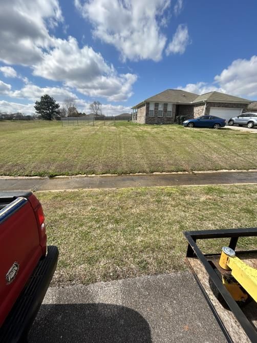 A man wearing a yellow hard hat is mowing his lawn