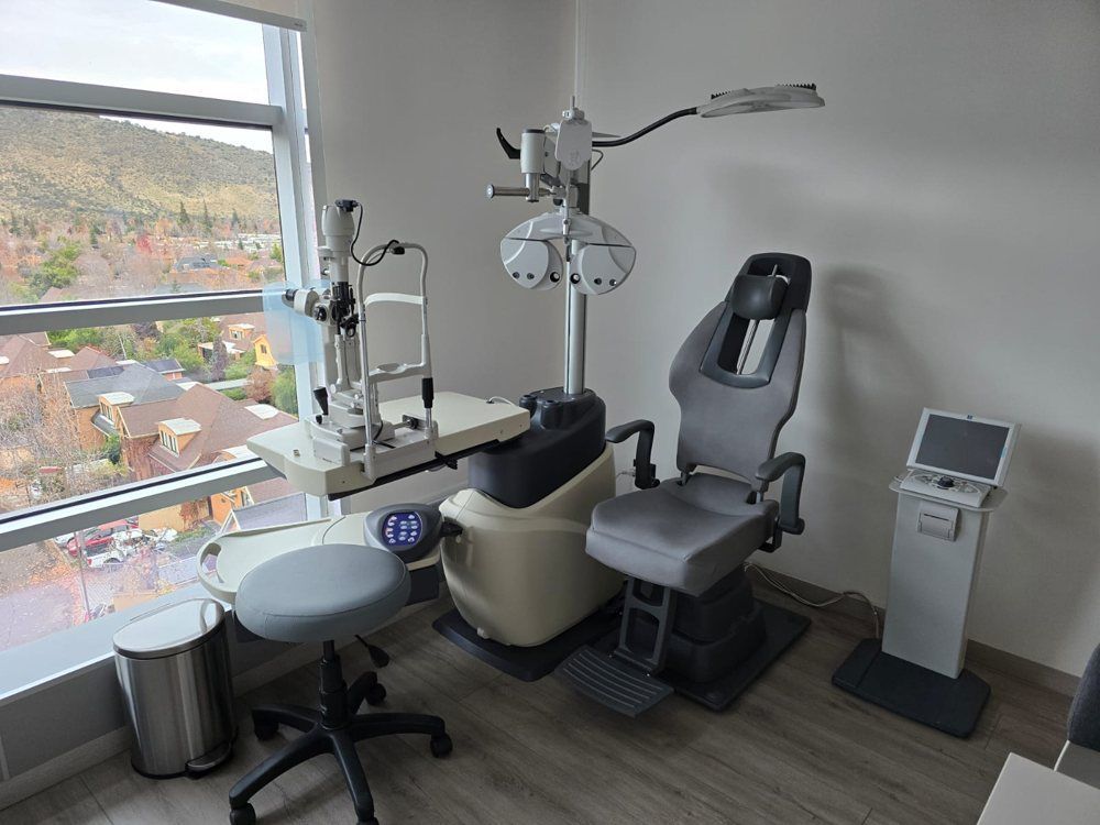 Consultorio moderno para examen de la vista con silla, taburete, instrumental y una gran ventana con vista a las colinas.