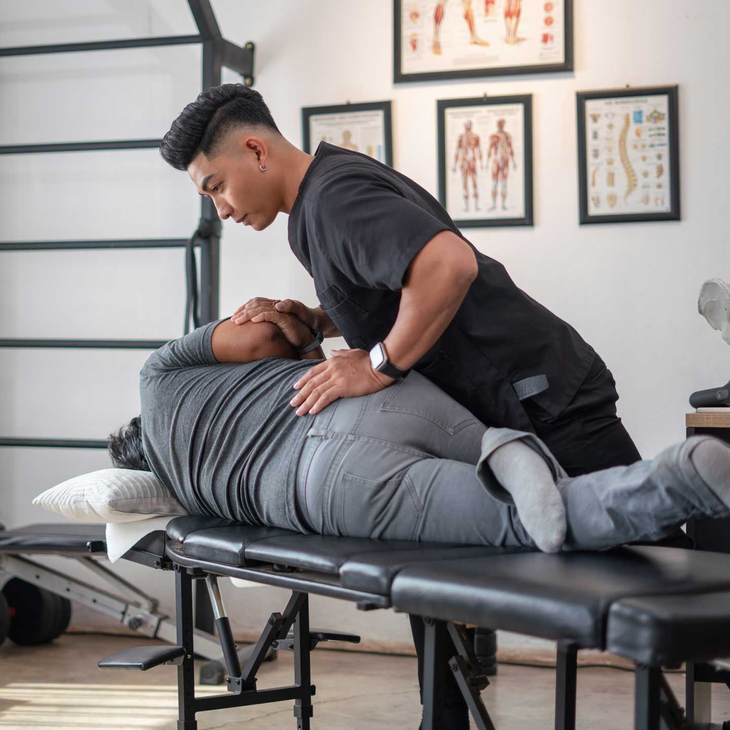 A chiropractor performs a spinal adjustment on a patient lying on their side on an examination table in a clinic.