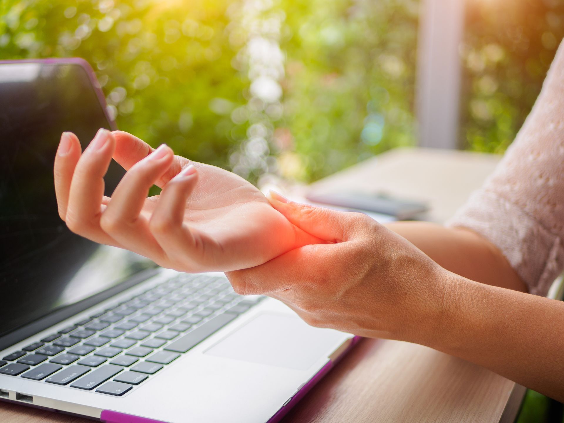 A person sitting at a laptop clutching their wrist, suggesting pain or discomfort.