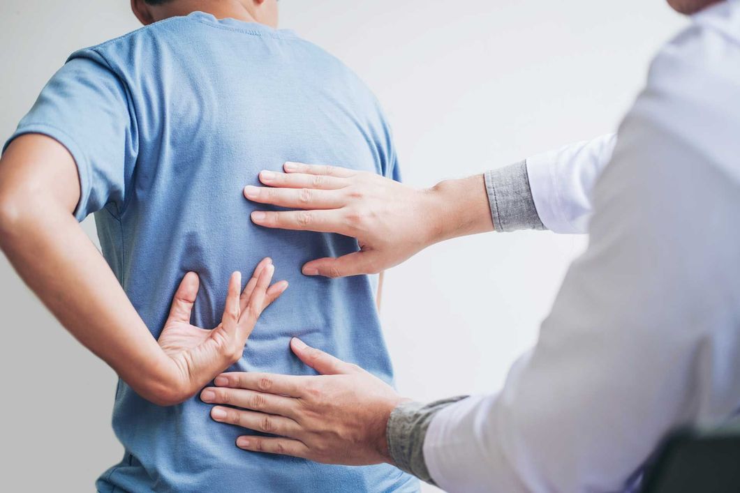 Doctor examining patient's back, palpating the lower back area. A healthcare professional in a white coat examines a patient’s back as they hold their lower spine.