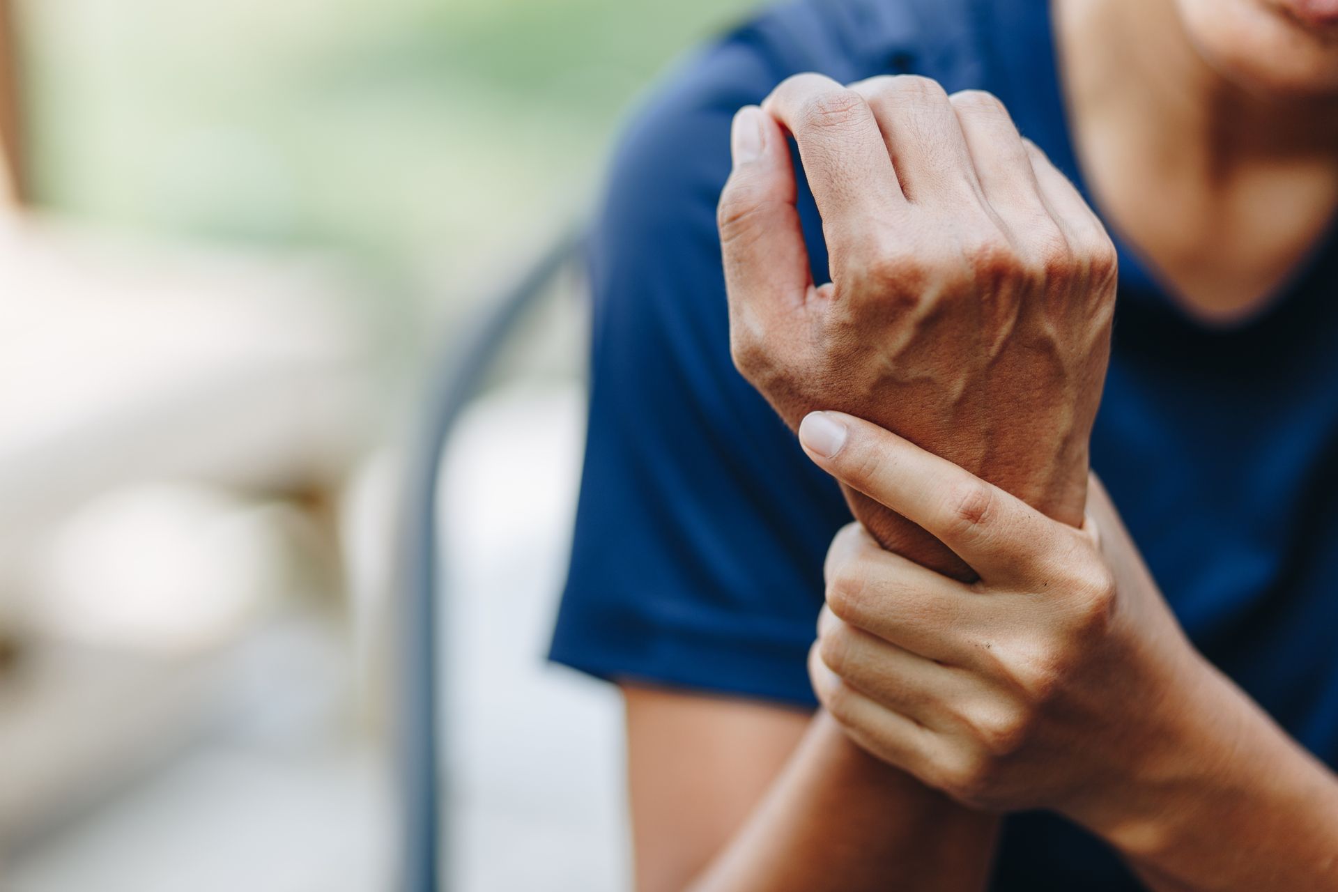 A person wearing a blue shirt holding their wrist, indicating pain or discomfort.