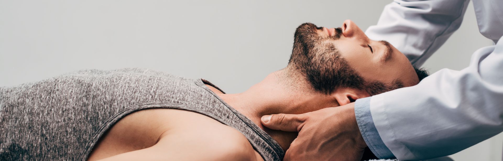Panoramic shot of a chiropractor massaging the neck of a man on a grey background.