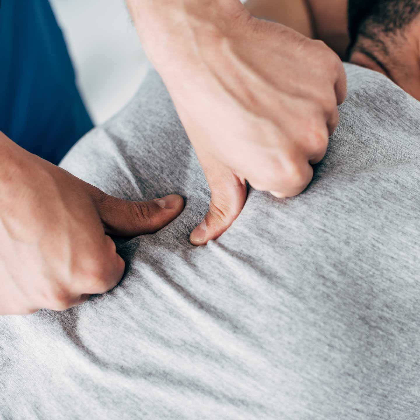 A close-up view of hands providing physical therapy, applying firm thumb pressure to a person’s upper back.