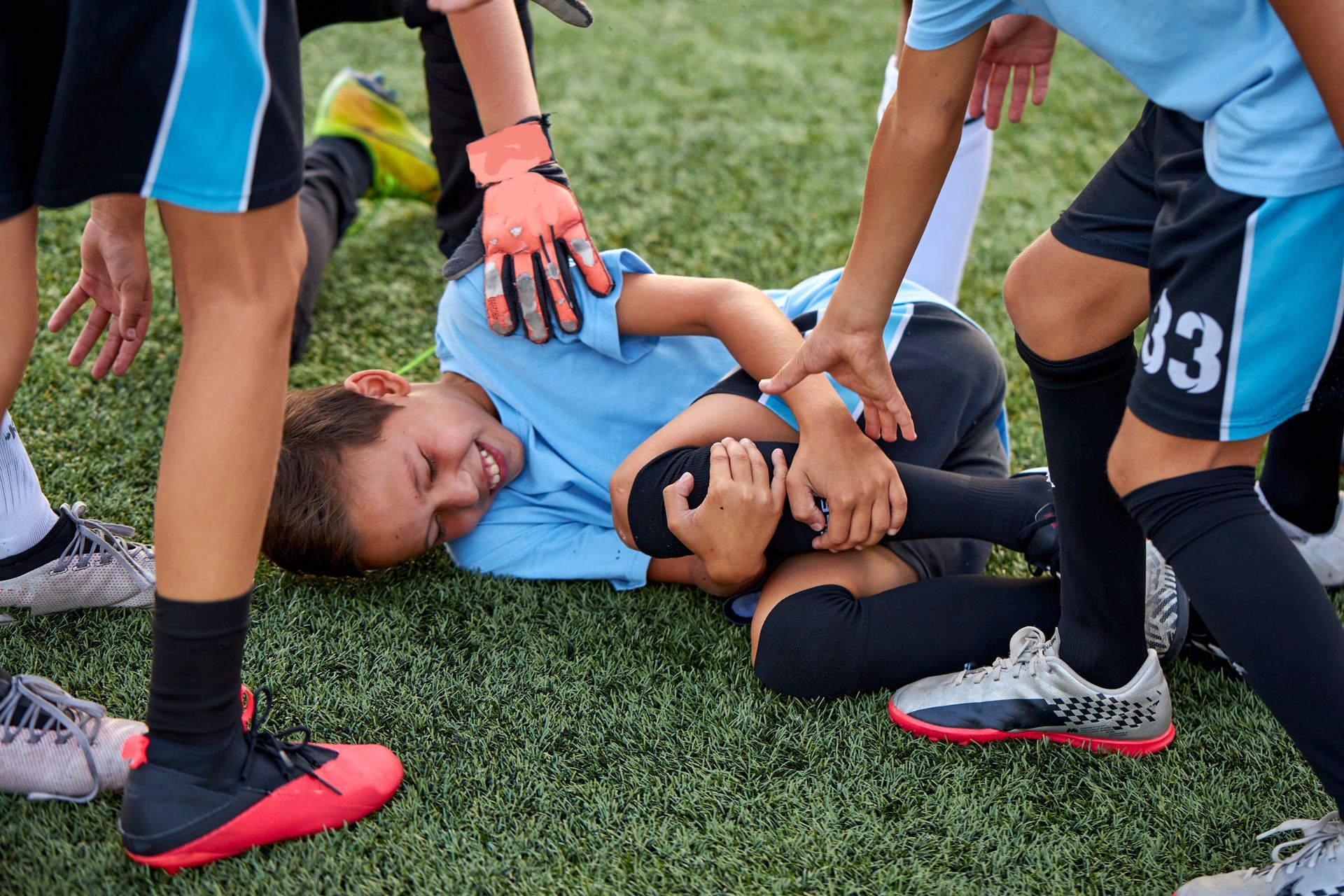 Teammates gather around a soccer player in a blue jersey sitting on the field clutching their injured knee.