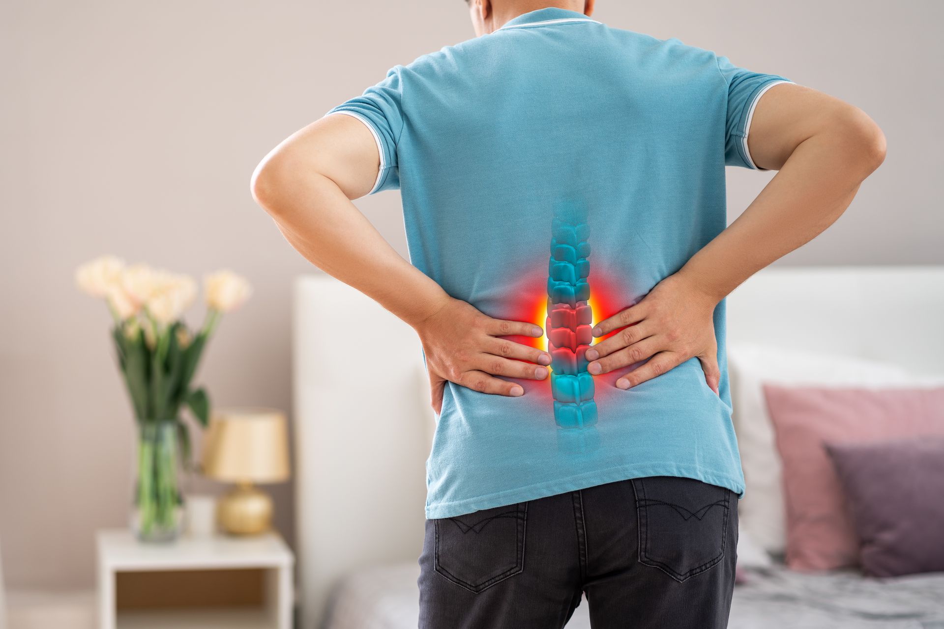 A person wearing a blue shirt stands in a room, holding their lower back where a glowing red area indicates pain.