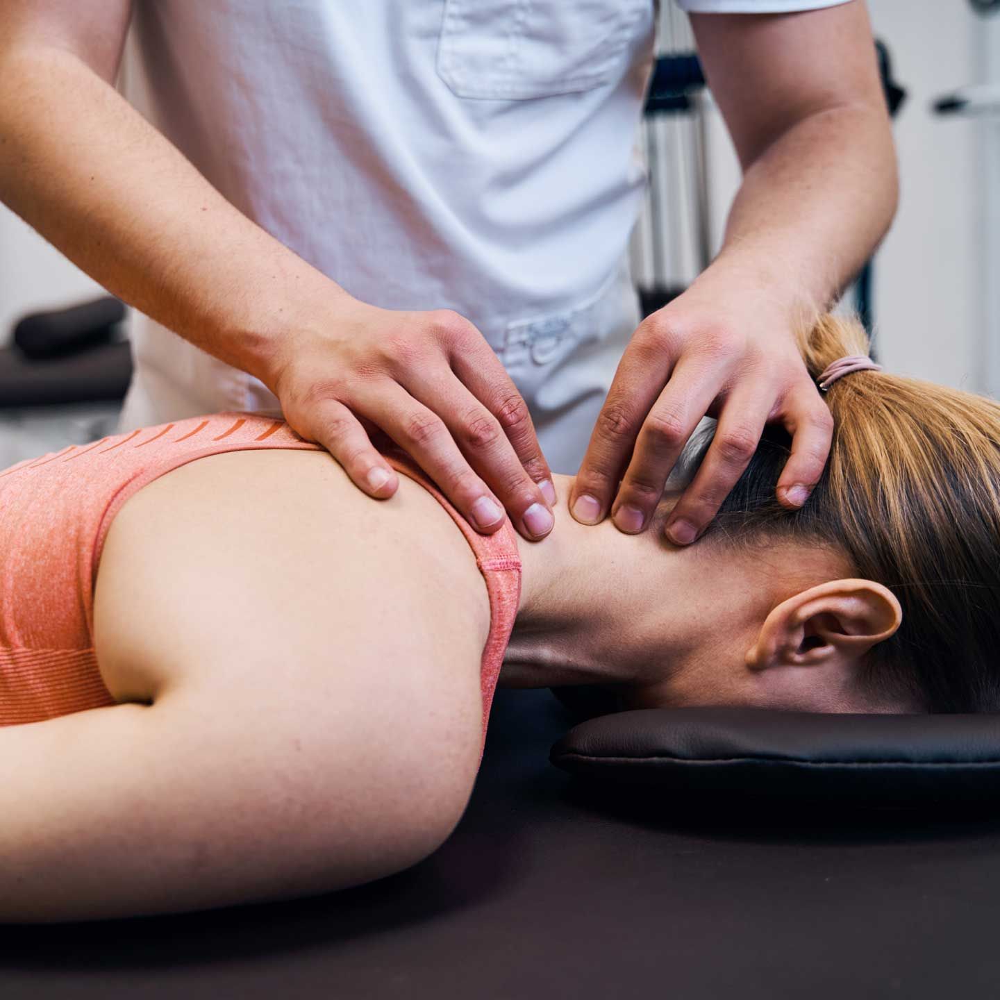 Therapist massaging a person's neck while they are lying down. A therapist in a white shirt performs a neck adjustment or massage on a patient lying prone on a medical table.