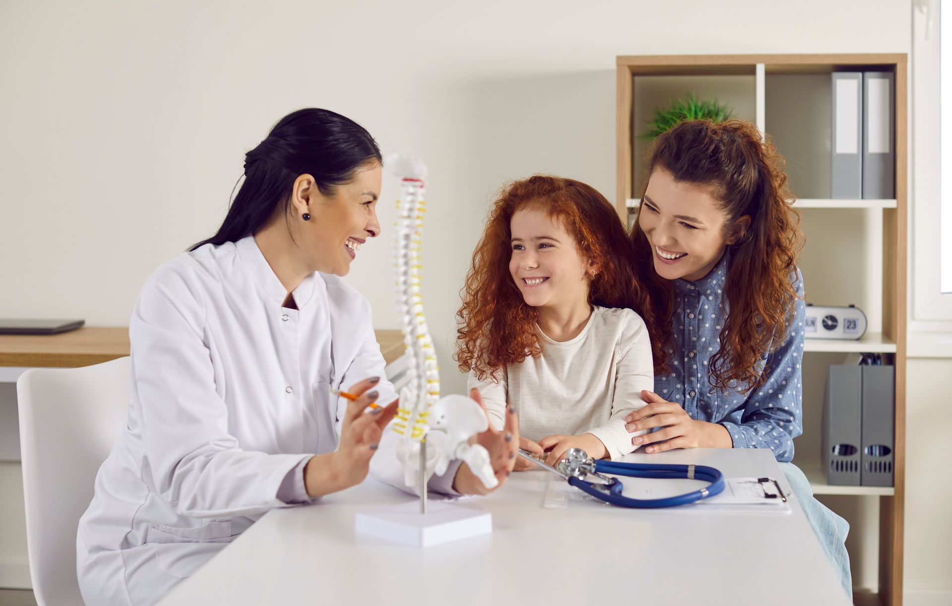 Doctor shows little girl anatomical model of spine standing on table in doctor's office. Doctor shows little girl anatomical model of spine standing on table in doctor's office.