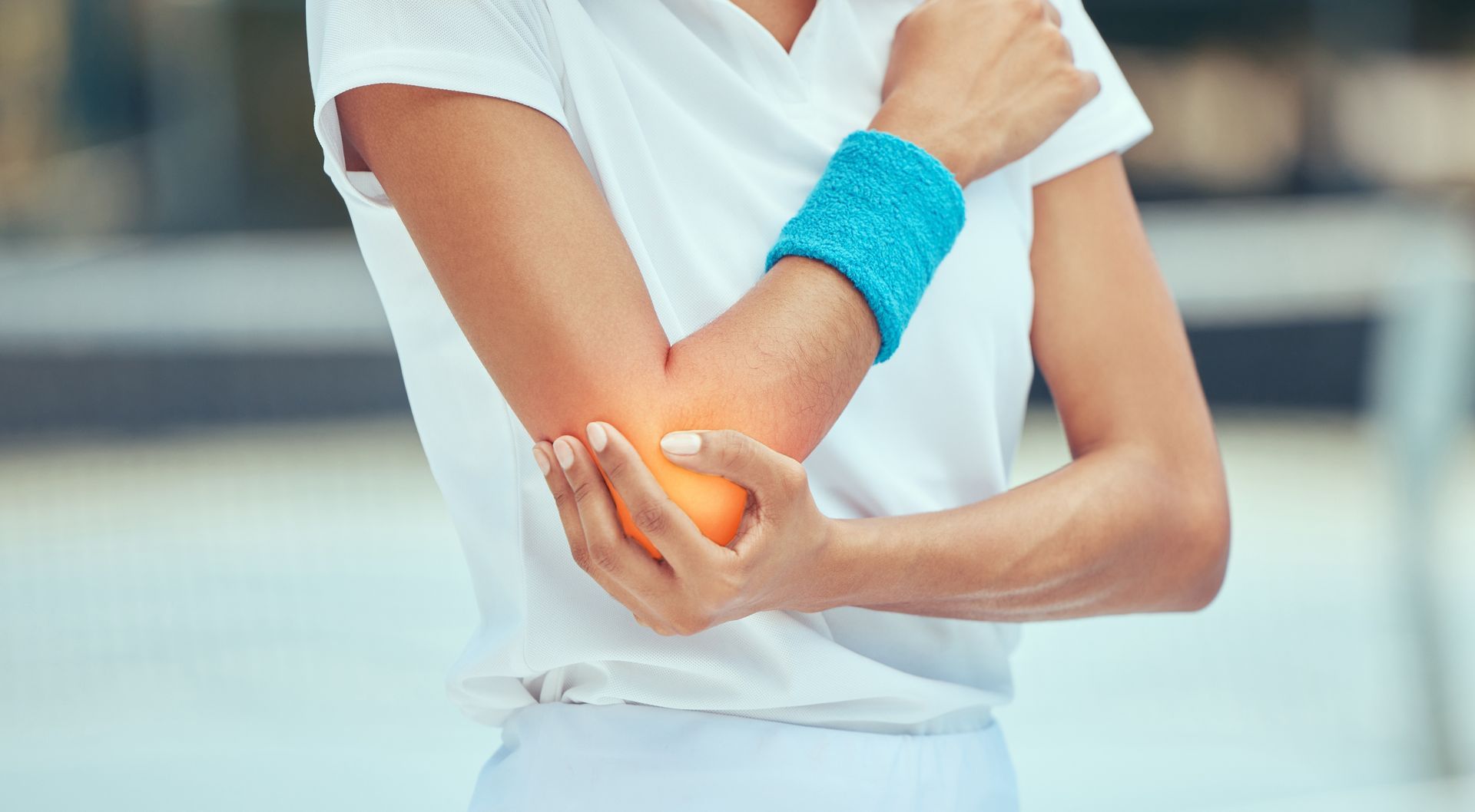 A person wearing a blue wristband holds their elbow, which is highlighted with a glowing orange light to indicate pain.